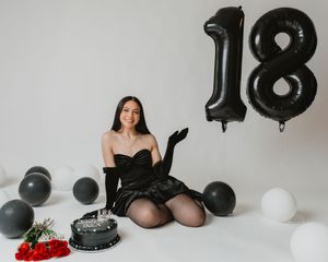 Young woman celebrates 18th birthday with black cake and number balloons.
