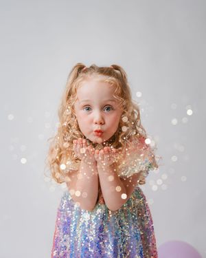 Adorable girl in iridescent sequin dress blowing glitter in studio portrait.