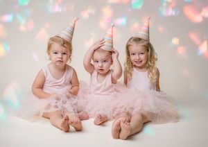 Three young girls in matching pink tutus and party hats pose together in a colorful birthday photo session.