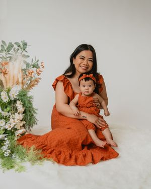 Mother and baby daughter in matching rust orange outfits posing beside a floral arrangement.