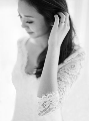 Black and white portrait of a bride in lace wedding dress delicately touching her hair.