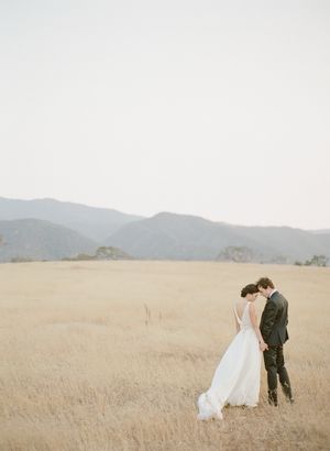 Bride and groom sharing tender moment in golden wheat field with mountain backdrop.