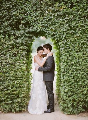 Bride and groom embracing in romantic ivy-covered archway in lush garden setting.