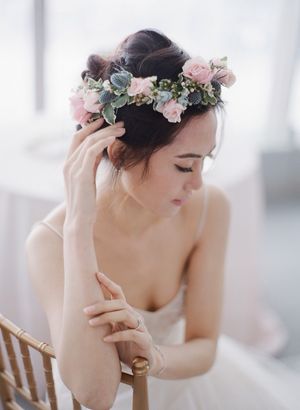 Beautiful Asian bride wearing a delicate pink and blue floral crown while seated in a chair.