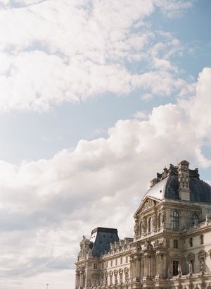 Elegant classical architecture of the Louvre Museum against a dramatic cloudy blue sky in Paris.