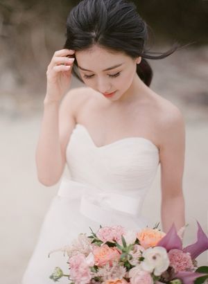 Elegant Asian bride in strapless sweetheart gown holds a pink and peach floral bouquet while looking down gracefully.