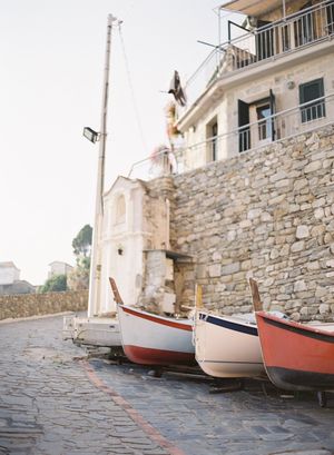 Two wooden boats resting on cobblestone street beside a rustic stone building in a Mediterranean coastal village.