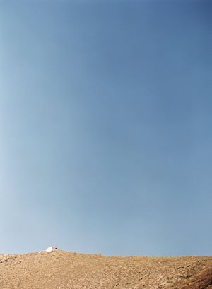 Minimalist landscape of a barren hillside with a small white structure against a clear blue sky.