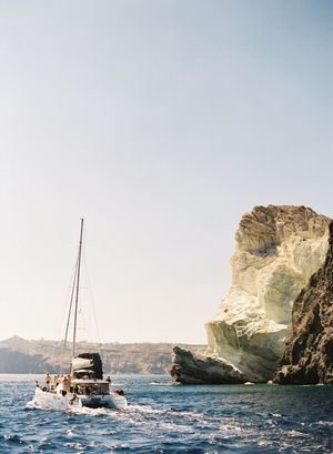 Sailboat with passengers cruising past dramatic white limestone cliffs on calm blue Mediterranean waters.