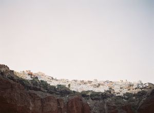 White-washed Greek village perched dramatically atop rugged volcanic cliffs at golden hour.