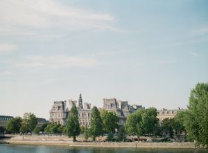 A scenic view of a grand Parisian building along the Seine River lined with lush green trees.