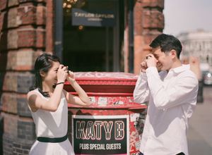 A couple playfully pretend to photograph each other near a red post box on a London street.