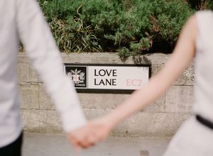 A couple holds hands while walking past a Love Lane EC2 street sign in London.
