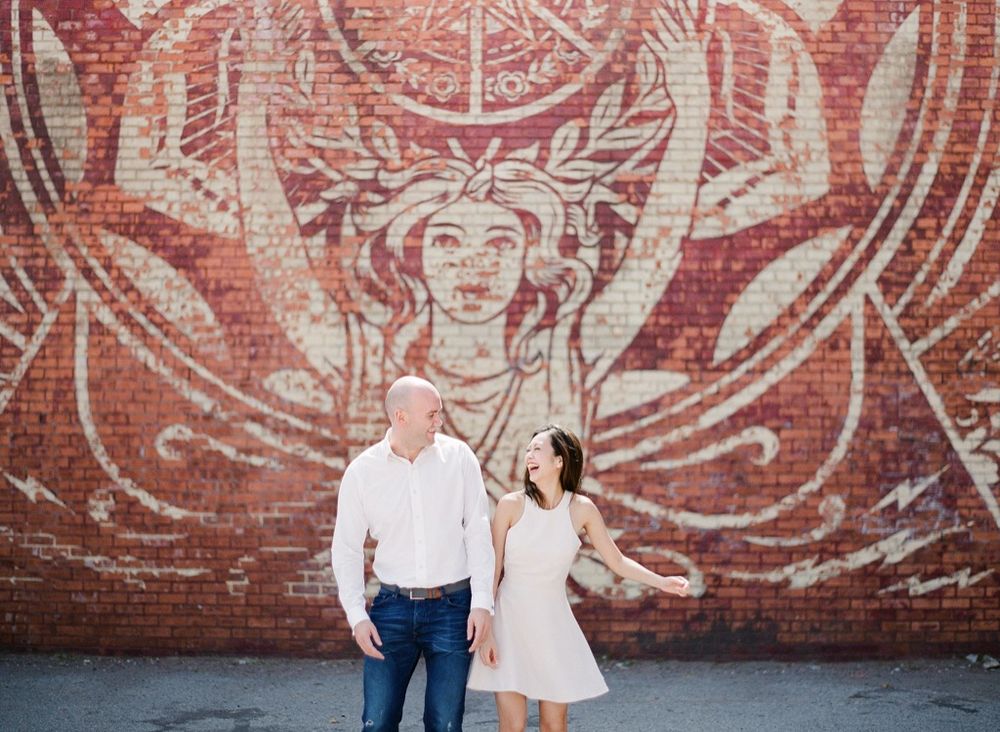 Couple posing in front of a large red brick mural wall in the city.