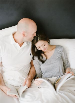Couple relaxing together on a white bed reading a magazine in a cozy setting.