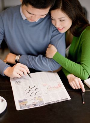 Couple doing a crossword puzzle together at a dark wooden table in a cozy setting.