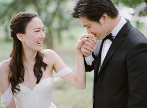 Bride laughing as groom kisses her hand during an outdoor wedding portrait session.