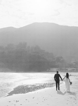 Black and white photo of bride and groom walking hand in hand on a beach.