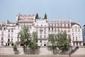 Classic Parisian architecture along the Seine River with elegant white Haussmann buildings and lush green trees.
