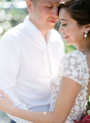 Intimate close-up of couple in soft natural light, bride wearing floral lace wedding dress with pearl earrings.