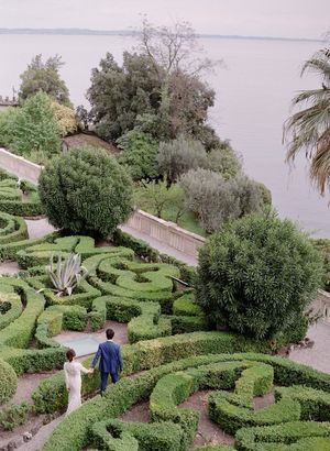 Aerial view of couple walking through an ornate garden maze near a lakeside estate.