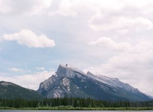 Scenic landscape of Mount Rundle rising above a pine forest under a cloudy sky.