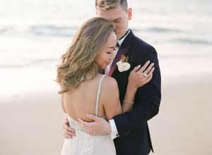 Bride and groom sharing an intimate embrace on a sandy beach with ocean waves in the background.