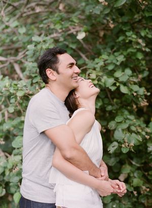 Couple embracing and laughing together outdoors with lush green foliage background.