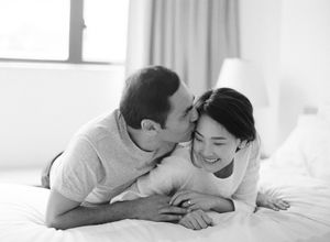Black and white photo of couple laughing and cuddling on a white bed.