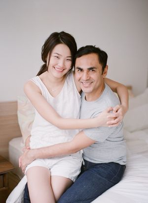 Smiling couple sharing a warm embrace while sitting together on a bed in a bright room.