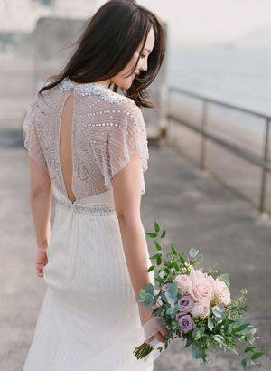 Bride in beaded open-back wedding gown holding a bouquet of pink roses and eucalyptus greenery.