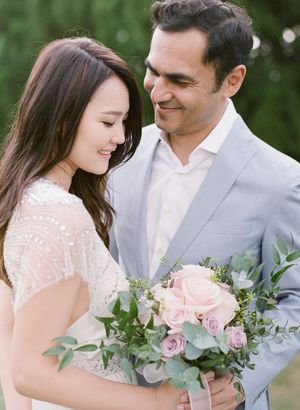Couple sharing a tender moment with bride holding pink roses and eucalyptus bridal bouquet outdoors.