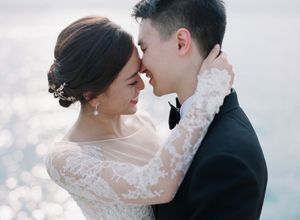 Bride and groom in elegant attire sharing an intimate moment by sparkling water.