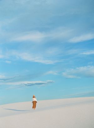 Lone woman standing on vast white sand dunes beneath a dramatic blue sky.