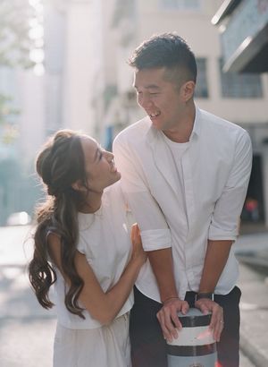 Happy Asian couple smiling at each other on a sunlit urban street during engagement shoot.