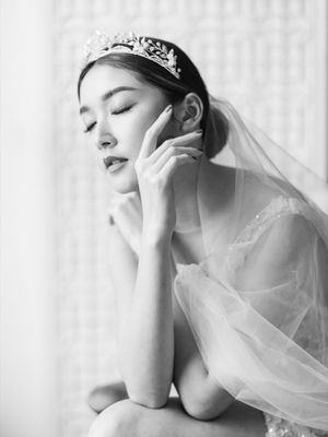 Black and white portrait of a serene bride wearing a tiara and veil by a bright window.