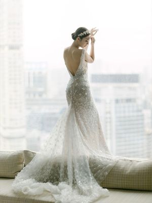 Bride in a backless beaded mermaid gown with a floral headpiece overlooking a city skyline.