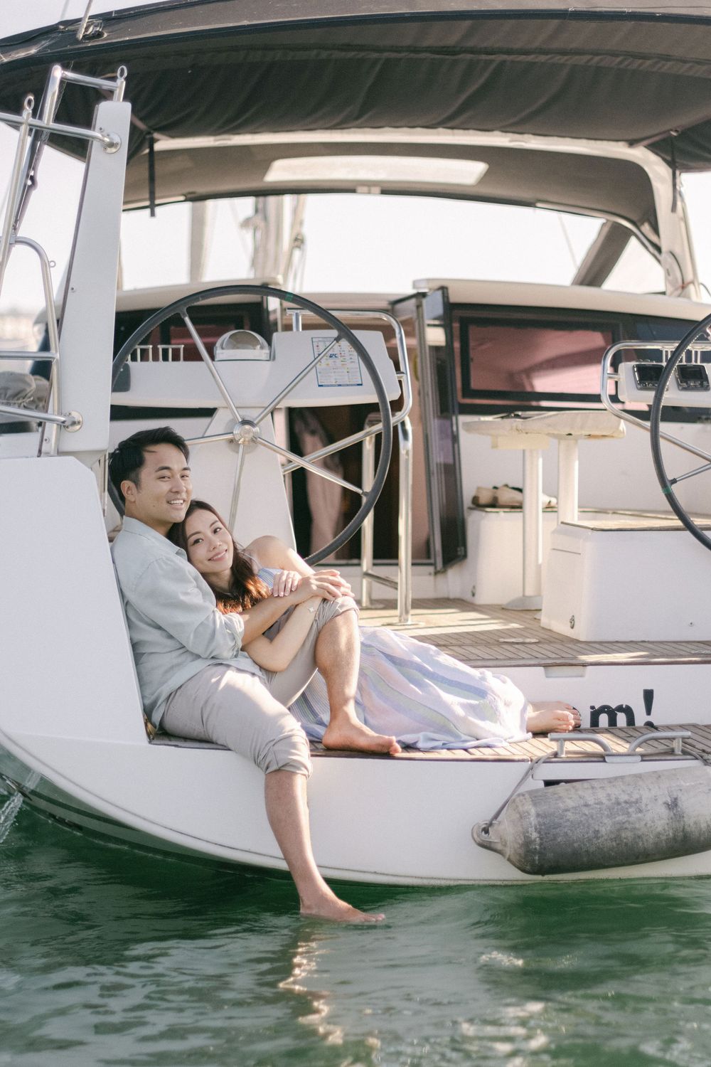 Couple relaxing together on the bow of a sailboat anchored in a sunny blue harbor.