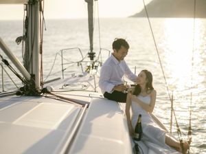 Romantic couple sharing champagne on white sailboat deck during glowing golden hour sunset.