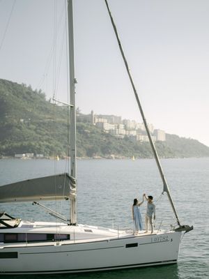 Couple dancing together on a sailboat deck with lush green hillside and calm harbor in background.