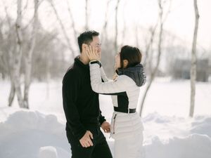 Romantic Asian couple sharing a tender moment in a snowy park with white birch trees.