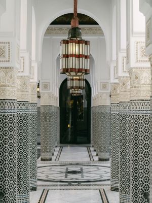 Ornate Moroccan hallway featuring intricate mosaic tiled columns, arched doorways, and a hanging lantern.