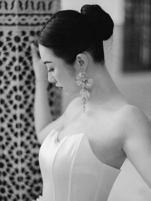 Black and white portrait of a bride with an elegant updo wearing floral drop earrings in a strapless gown.