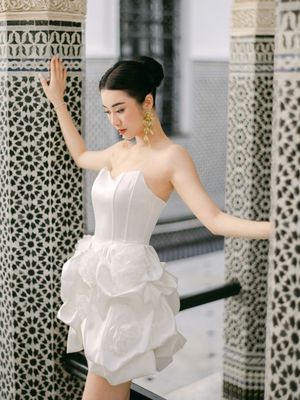 Bride in a strapless white ruffled mini dress poses against ornate Moroccan mosaic tiled columns.