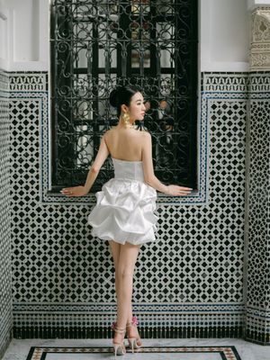 Bride in a strapless white bubble mini dress stands before an intricate Moroccan mosaic tiled wall.
