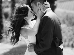 Black and white romantic photo of a bride and groom sharing a kiss outdoors on a windy day.