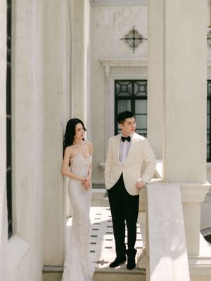 An elegant couple poses in wedding attire among white marble columns in a grand venue.