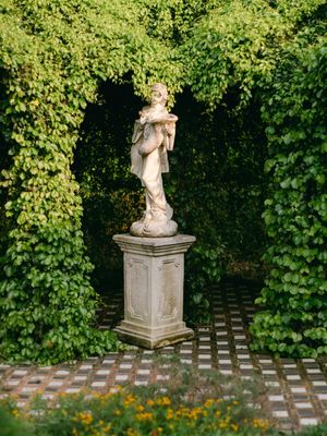 A classical stone statue of a woman stands on a pedestal surrounded by lush green ivy.