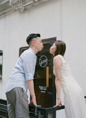 Couple sharing a playful almost-kiss moment outside a charming white brick building.
