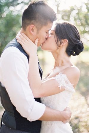 Asian bride and groom share a romantic kiss outdoors in soft golden bokeh light during their wedding day.